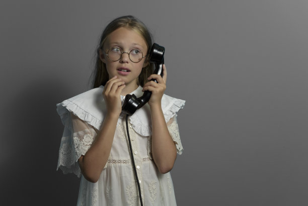 一个拿着手机的少女的肖像。过去的沟通。复古。旧的手机。灰色的背景。图片下载