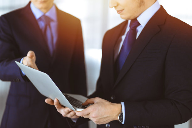 商务人士站在阳光明媚的现代办公室里，在会议上讨论演示文稿。不知名的商人和同事在笔记本电脑上搜索一些信息，律师在谈判。团队合作及伙伴关系理念图片下载