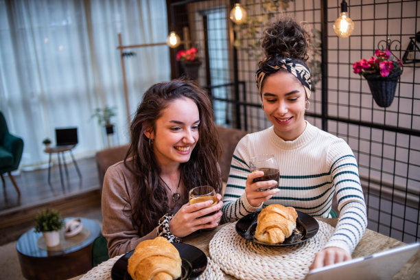 两个女人，朋友，坐在家里的酒吧里，吃早餐，喝咖啡，用平板电脑上网图片下载