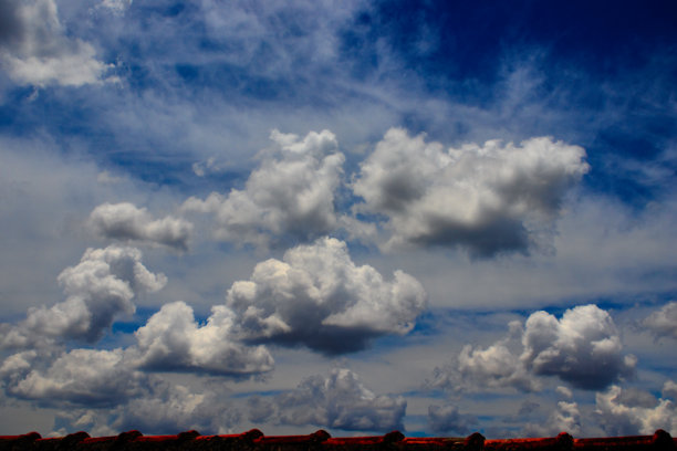 一群白色的积云，被正午的光线照亮，漂浮在屋顶上，蓝色的天空被卷层云覆盖。图片下载