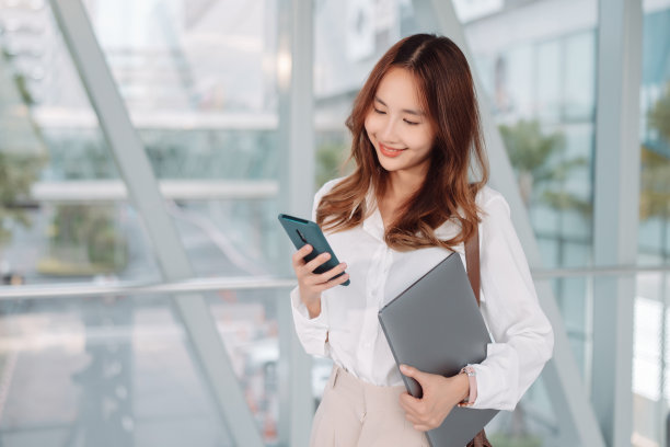 美丽的亚洲女商人使用智能手机，散步享受微笑，在办公大楼附近的现代城市通勤图片下载