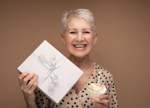 美丽快乐的老年女性纸杯蛋糕，蜡烛和礼盒。图片下载