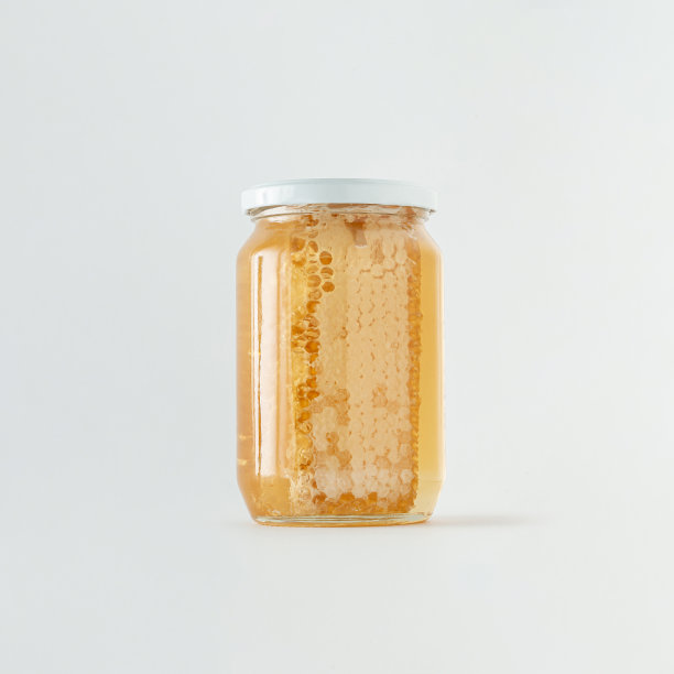 蜂巢和金色的蜂蜜在玻璃罐上孤立的粉彩白色背景。替代疗法或者吃生的健康的甜食。天然养蜂产品的最小创意概念。图片下载