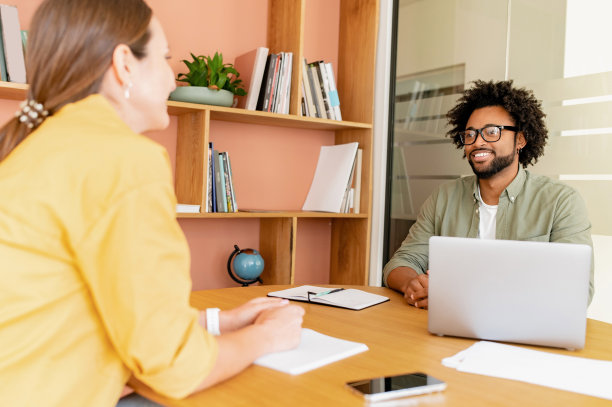 男人和女人站在现代化的办公室里对着笔记本电脑看对方，同事们讨论项目，两个同事头脑风暴图片下载