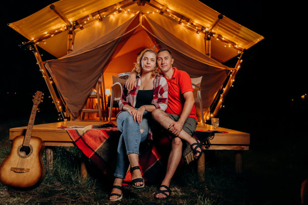快乐可爱的情侣在晚上舒适的篝火旁放松。户外休闲休闲的豪华露营帐篷。生活方式的概念图片下载