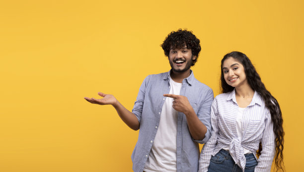 快乐的印度夫妇指着张开的手掌，男子演示无形的物体，显示复制空间，全景图片下载