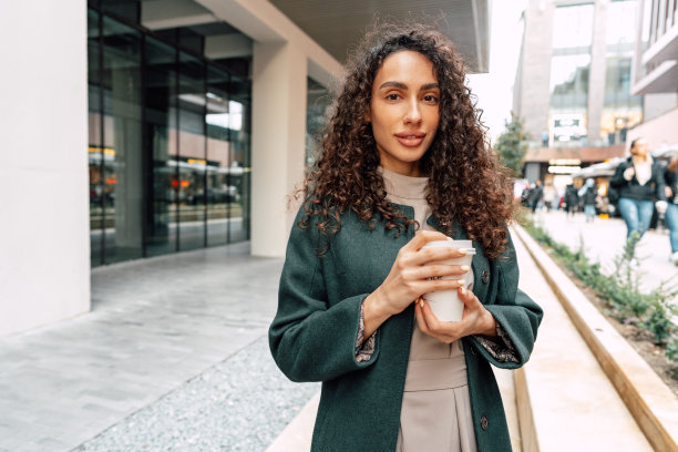 年轻开朗的女人拿着咖啡杯走在城市里图片下载