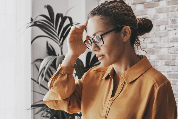 头疼一名年轻女子的特写照片，她坐在沙发上，闭着眼睛，摸着自己的头，患有偏头痛。商务办公背景生活方式人士图片下载