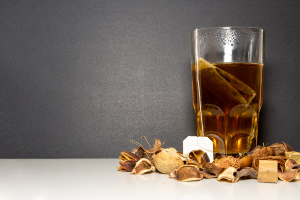 黑色背景的白色桌子上有一个水晶杯，里面有一个茶包，周围有干花。图片下载