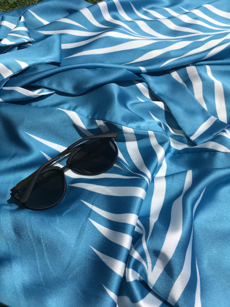 夏日静物:一件带墨镜的蓝色丝绸连衣裙。夏天集。一件蓝色的丝绸连衣裙，上面缀着白色的棕榈叶，飘逸在地上。图片下载