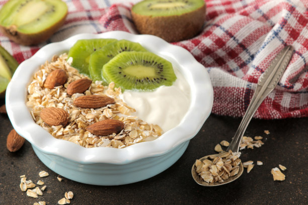 希腊白酸奶，猕猴桃杏仁和燕麦片放在深棕色的桌子上。早餐。健康的食物图片下载