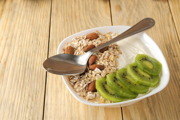 希腊白酸奶，猕猴桃杏仁和燕麦片放在天然木桌上。早餐。健康的食物图片下载