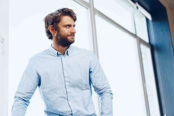 一个穿着休闲衬衫的白人男子站在窗户附近的肖像图片下载