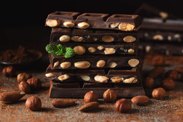 黑牛奶巧克力，黑色背景上撒有可可粉的坚果。图片下载