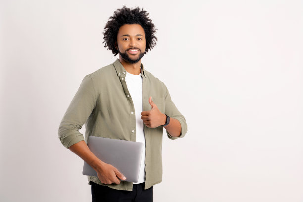 微笑卷曲的30岁男子在便装站与笔记本电脑隔离在白色，显示大拇指图片下载