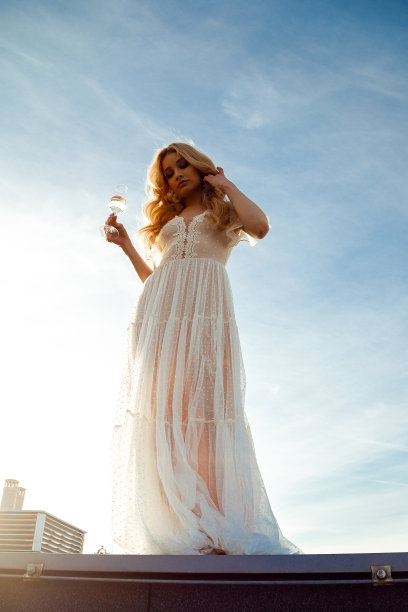 下面的全长照片，浪漫的女孩穿着美丽的裙子，站着向下看，拿着一杯饮料，天空为背景。时尚的外观，在屋顶，天空，巴黎城市景观放松图片下载