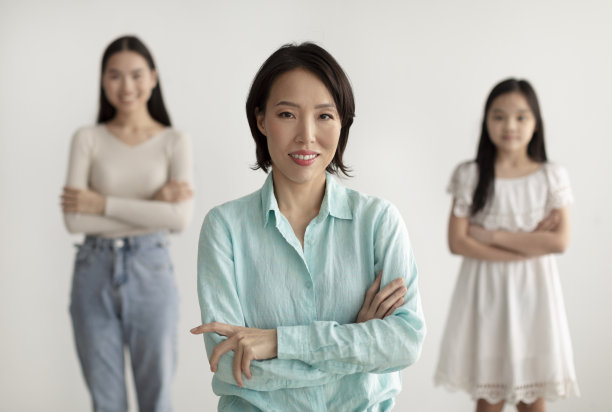 美丽成熟的亚洲女人与她的成年女儿和孙女交叉双臂，对着镜头微笑图片下载