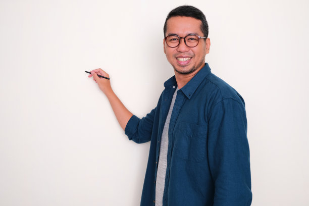 一名亚洲男子微笑着在他身后的空白处用笔写字图片下载