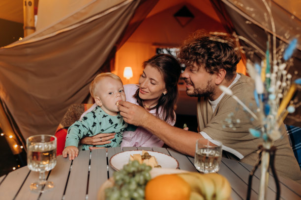 幸福的家庭和可爱的宝宝一起吃晚餐，一起在夏天的晚上在舒适的篝火旁露营。户外休闲休闲的豪华露营帐篷。生活方式的概念图片下载