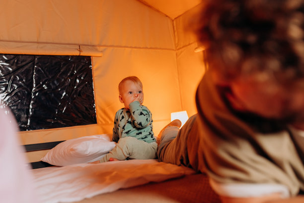 幸福的家庭，可爱的宝宝玩耍，夏天晚上躺在床上，一起度过舒适的豪华露营时光。户外休闲休闲的豪华露营帐篷图片下载
