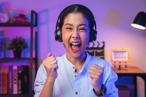 年轻的亚洲女子戴着耳机，双手举起双臂，握紧拳头，表现出强大的力量，庆祝胜利，表达成功。图片下载