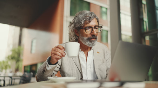 成熟的商人，戴着眼镜，穿着灰色夹克，坐在咖啡馆里。中年经理成功男士坐在户外的咖啡馆里图片下载