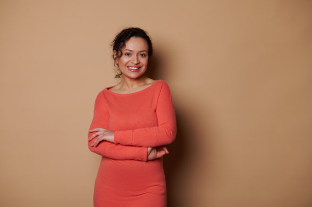 有吸引力的女人微笑着咧嘴笑着看着相机，摆好手在米色背景图片下载