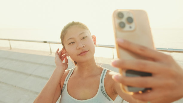 在晨光中，亚洲女孩在现代建筑背景上站在堤岸上自拍图片下载
