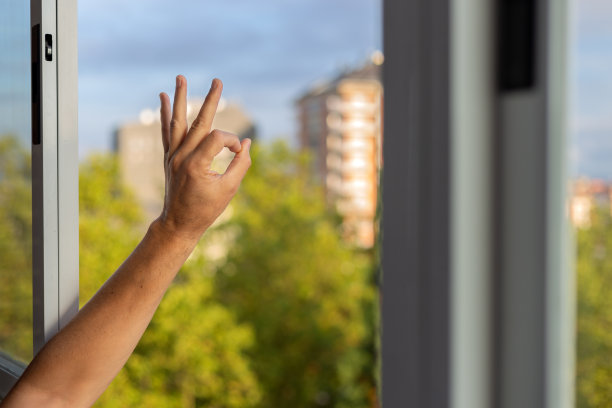在新的阳光明媚的早晨，男子在阳台窗户上用左手做ok标志。新的家园，新的抱负，新的目标。图片下载