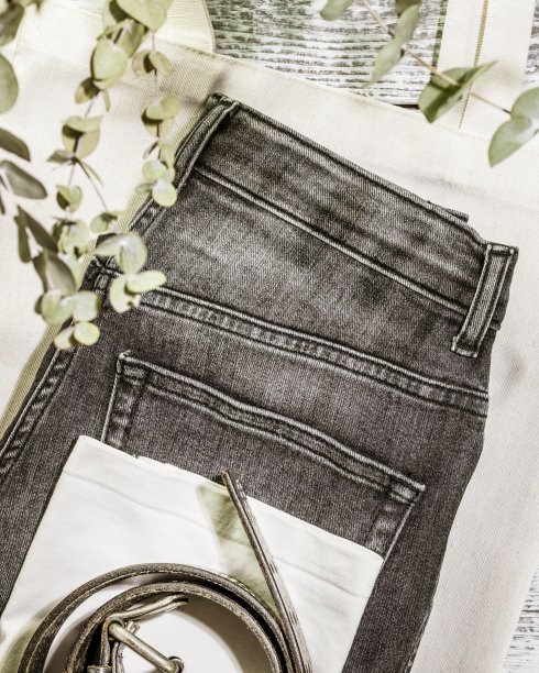 牛仔裤，t恤，腰带在纺织袋上的木制背景与树叶和阴影图片下载