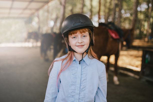 小女孩在马厩里摆姿势，背景是马。图片下载