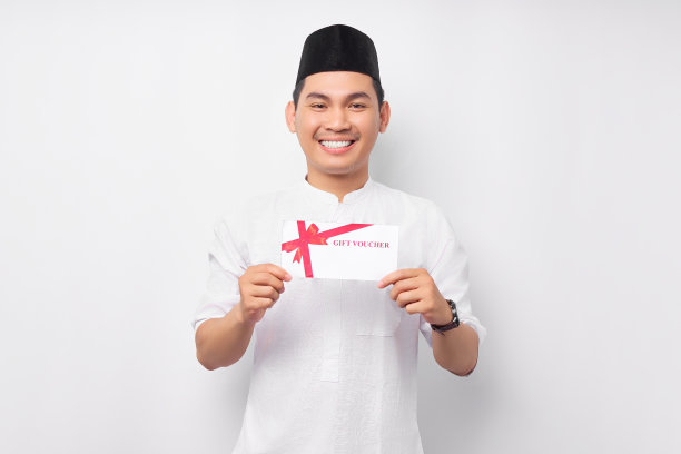微笑的年轻亚洲穆斯林男子拿着礼券券在白色背景上孤立的手。人们信仰伊斯兰教的生活方式观念。庆祝斋月并炸死了穆巴拉克图片下载
