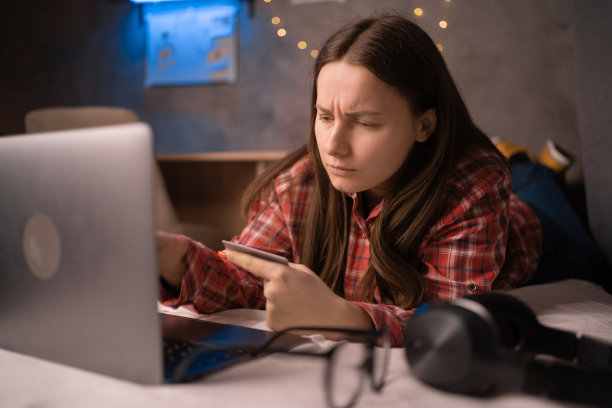 顾客在宿舍房间的床上用信用卡和笔记本电脑网购。图片下载