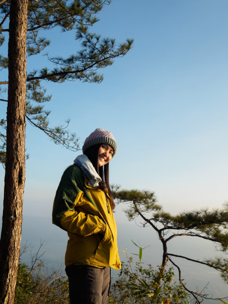 亚洲游客年轻女子穿夹克，长裤，戴毛线帽。站在悬崖边上，微笑着看完雾气缭绕的日出，在普克杜登国家公园图片下载