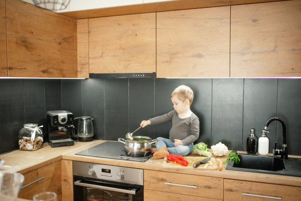 可爱的金发男孩蹒跚学步煮蔬菜汤，混合在锅里，坐在厨房抽屉上的炊具附近。小帮手学做饭图片下载