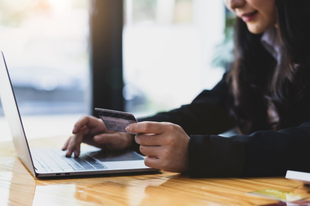 女人拿着信用卡，用着笔记本电脑。网上支付和网上购物的概念。图片下载