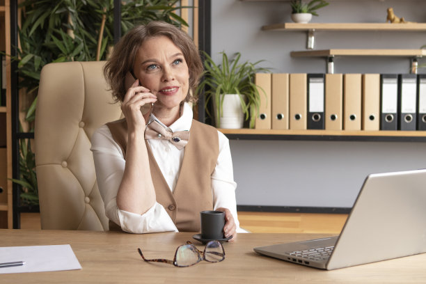 一个穿着米色西装的女商人在办公室工作。喝咖啡，用电脑打字图片下载