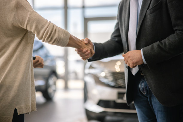 图为，在汽车销售店的室内，女顾客正在与西装革履的男性汽车销售者握手图片下载