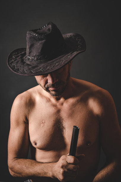 白人男性牛仔在黑色背景前戴着牛仔帽，手持猎枪图片下载