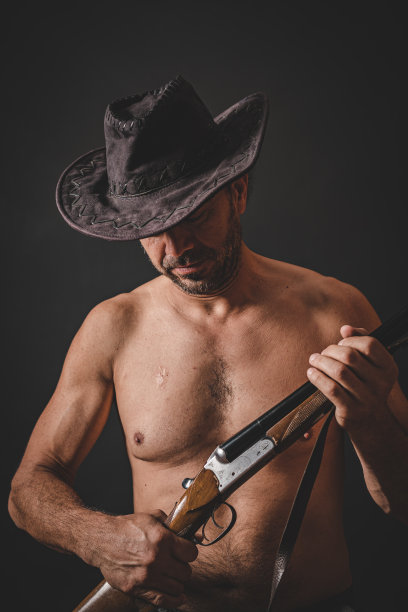 白人男性牛仔在黑色背景前戴着牛仔帽，手持猎枪图片下载