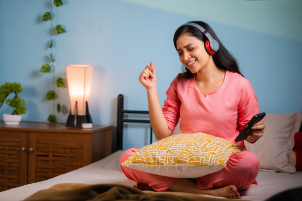 晚上在床上跳舞，一边听着手机上最喜欢的歌曲，一边享受年轻女孩的快乐——娱乐、周末假期和自我护理或健康的概念。图片下载