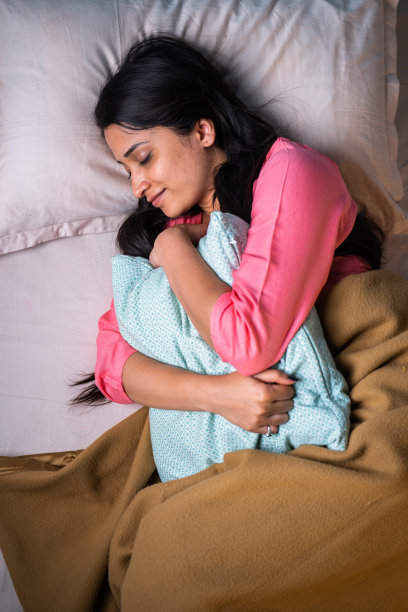 垂直俯视图拍摄的年轻女孩舒适地睡在床上抱枕头在晚上-想象的概念，舒适和自我照顾或健康。图片下载