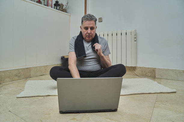 一个男人看着笔记本电脑在家里锻炼图片下载