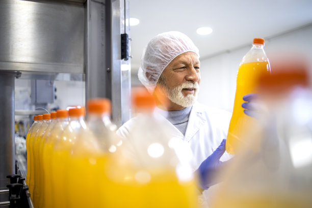 有经验的工人拿着PET瓶，在装瓶厂对橙汁进行目视检查。图片下载