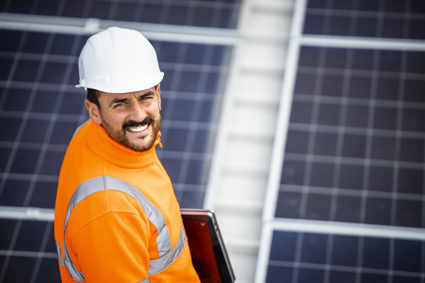 近距离观察太阳能公司工人站在大型太阳能发电厂。背景光伏电池模块，将阳光转化为电能。图片下载