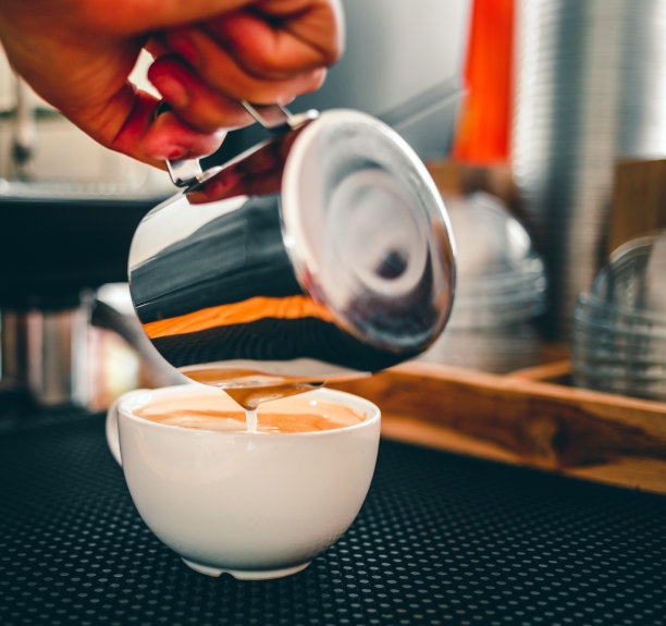 特写的手，一个专业的咖啡师在咖啡店把蒸牛奶倒进咖啡杯制作拿铁菜单图片下载