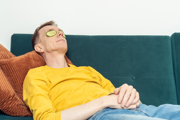 成年男子躺在沙发上，眼罩是新鲜的黄瓜片在客厅。黑眼圈面膜。图片下载