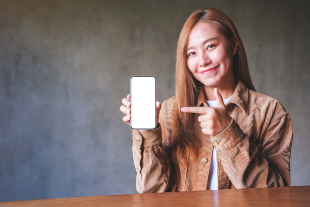 一个年轻女子拿着、展示并指着一部手机的模型图，手机的屏幕是空白的图片下载