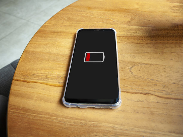 屏幕上低电量图标的智能手机特写。在木桌背景上图片下载