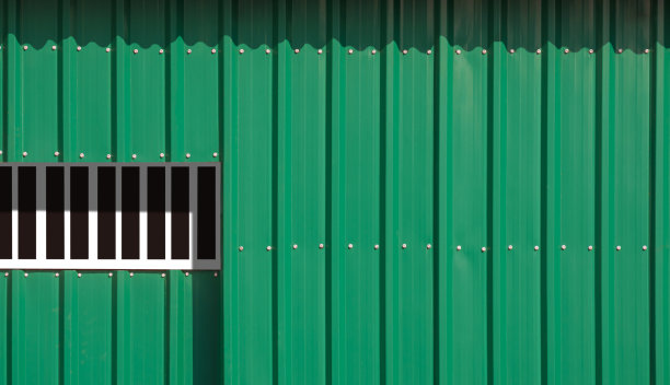 阳光和阴影在绿色波纹钢墙背景的滑动入口门表面图片下载